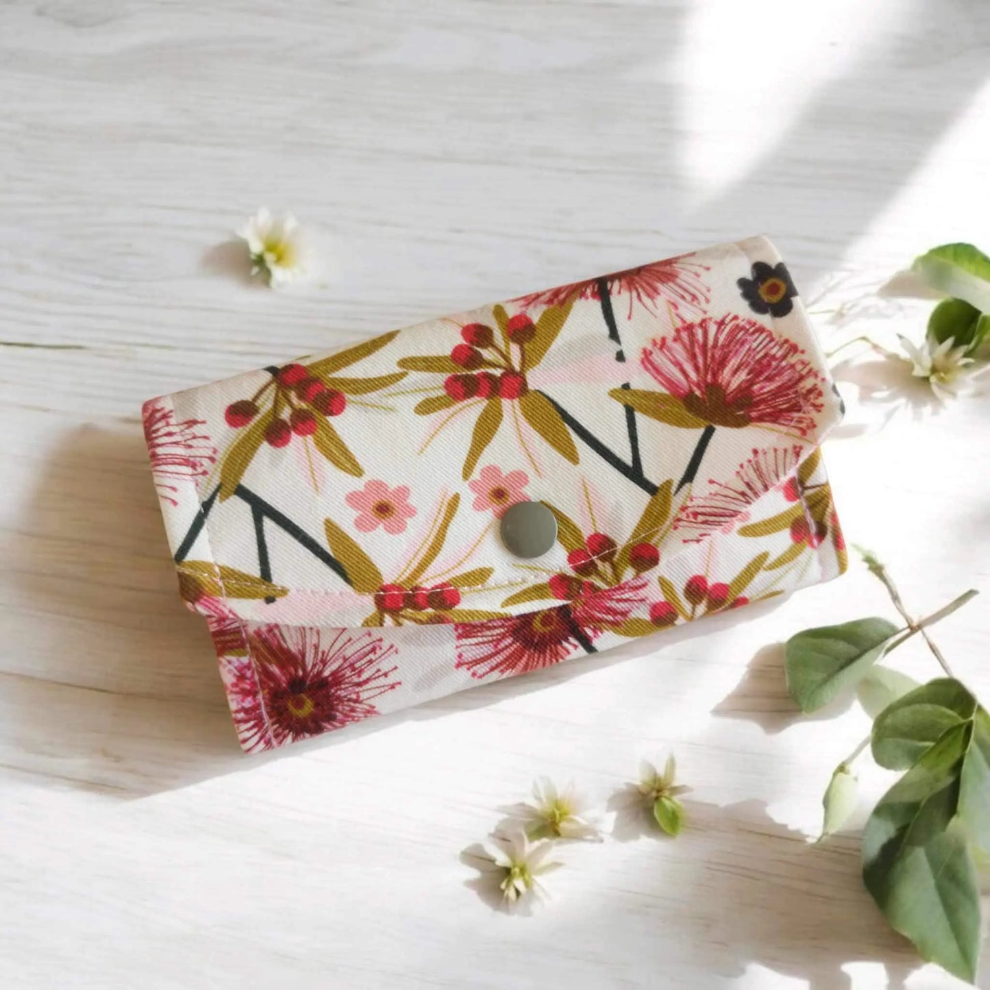 Australian floral themed coin purse/ small glasses case. The purse/ glasses case measures 14cm x 8cm. Colours of fabric design include white, pink, red-pink, green and black. Closure is 1 x grey kam snap.