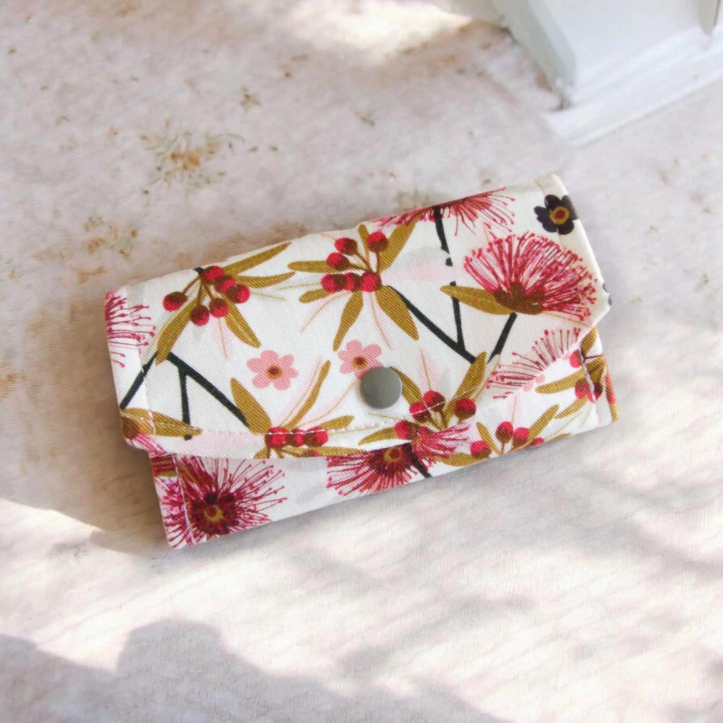 Australian floral fabric coin purse/ small glasses case on a white background. The red-pink flowers and berries, with the green leaves and dark stems look stunning set against the white fabric background.