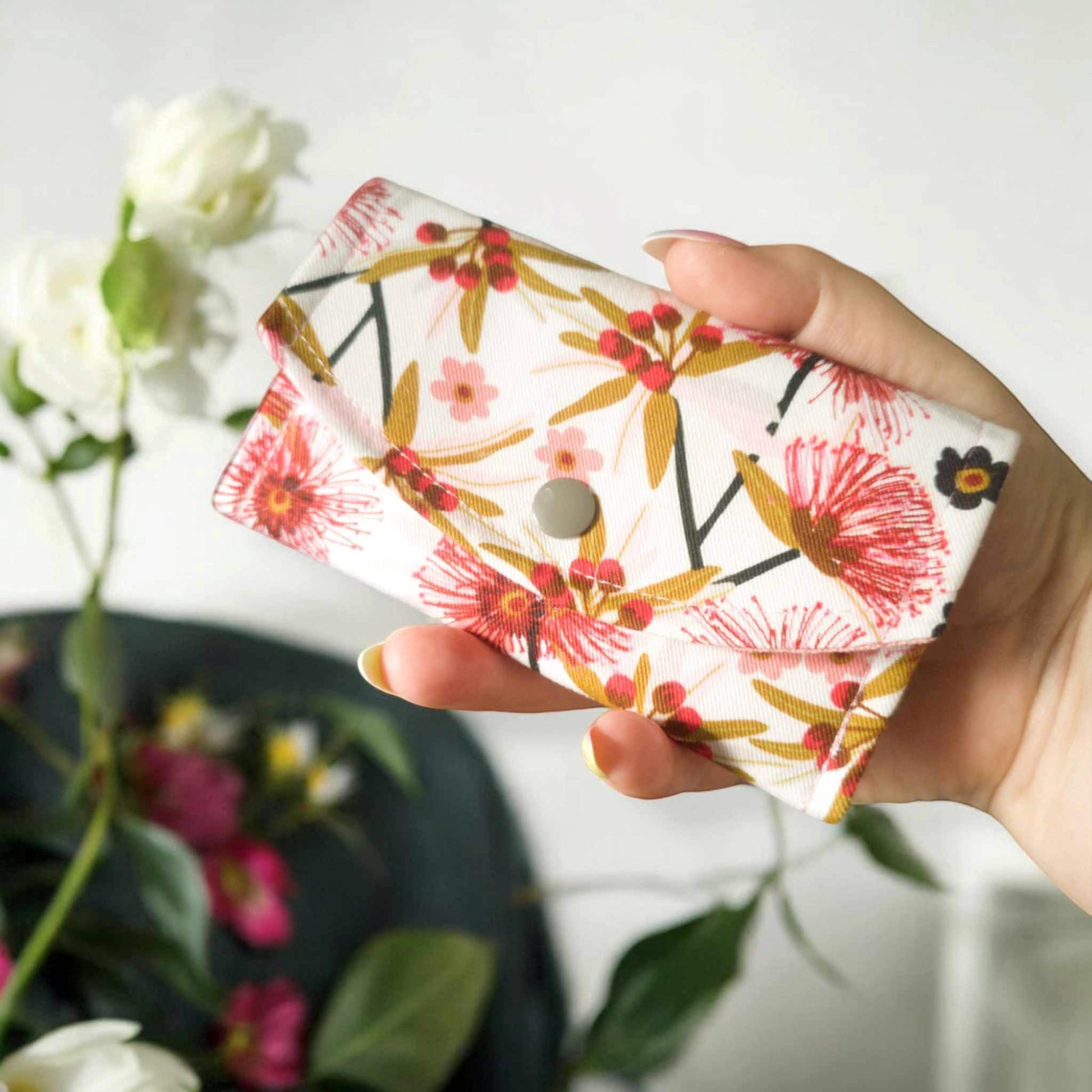 Australian fabric floral coin purse/ small glasses case being held in hand to show size - 14cm x 8cm. With a floral blurred background.